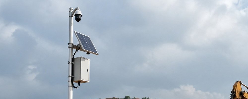 Solar powered CCTV camera pole at a construction site with solar panel and battery enclosure above safety fencing