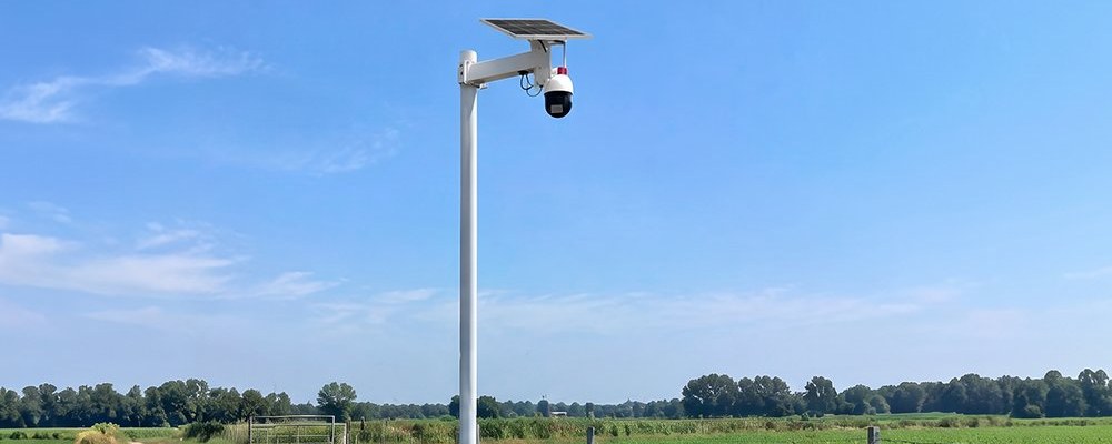 Pole-mounted solar power system for farm security cameras: solar panel, camera and sealed battery box on one pole beside a farm field